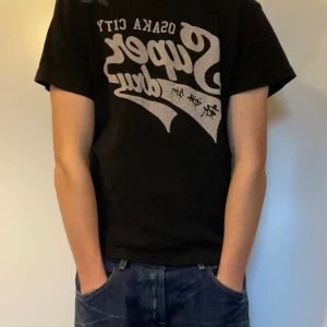 Svart Superdry t-shirt med tryck - Svart t-shirt från Superdry med stort vintageinspirerat tryck i grått på bröstet | Siffran 76 broderad på axeln | Skön passform | Storlek S