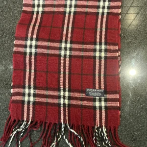 Röd halsduk från Burberrys - Röd halsduk från Burberrys med vita och mörkröda linjer. Den passar med nästan alla outfits, perfekt för din Grisch outfit. Riktigt snygg och fin.