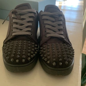 Gråa skor med röd sula - Säljer ett par gråa sneakers med grå snörning och coola gråa nitar på tån. Skorna har den ikoniska röda sulan och är tillverkade i mocka. Perfekt för dig som vill sticka ut med en edgy och lyxig stil. Pris är inte hugget i sten