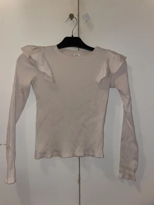 Beige ribbad topp med volang från Zara - Supersöt beige långärmad topp från Zara med ribbad struktur och volangdetaljer på axlarna.