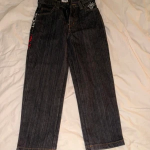 Your Local Dealer jeans med tryck - Unika mörkgrå jeans med bred passform från Your Local Dealer. Baksidan har ett stort, detaljerat tryck i rött, vitt och svart med texten 'Your Local Dealer' och grafiska mönster. Klassisk femficksmodell med raka ben och coola detaljer längs sidorna. Dessa ligger även uppe på vinted, dom är tyvärr alldeles för små för mig. Dom går ner till halva smalbenet på mig som är 163 så dom skulle passa någon som är kortare! 🫶🏼 Jag tar gärna fram mått för den som önskar!