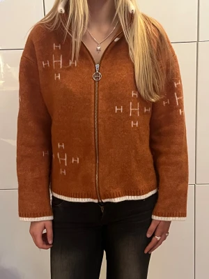 Rostbrun/Orange stickad cardigan kofta från Hést - Säljer en  rostbrun/orange stickad cardigan kofta från Hést med vit kant och dragkedja framtill. Koftan har långärmade ärmar, ribbad krage och ett unikt mönster i vitt. Koftan är i mohair och merinoull.  Perfekt för dig som gillar chill och snygg stil.