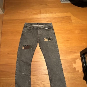 Monten jeans  - Säljer ett par grå jeans med slitna hål på låren där camouflage-tyg syns under. Modellen har klassisk femficksdesign och raka ben. Jeansen har en cool streetstil och passar dig som gillar edgy detaljer.