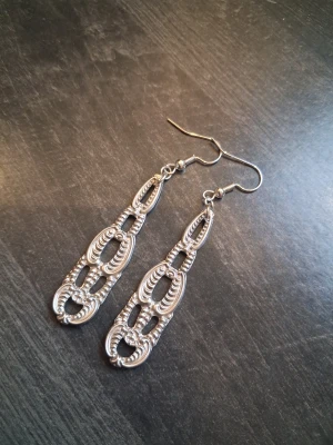 Handgjorda örhängen återbruk  - Unika och snygga örhängen skapade av bestick i nysilver. Detaljerad, länkad design och böjda former. Hängande modell som ger ett coolt statement till din look. Perfekta för dig som gillar att sticka ut med accessoarer. Öronkroken är nickelsäker och aldrig använda 