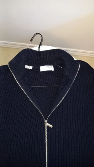 kofta från Selected Homme - Snygg mörkblå stickad kofta från Selected Homme med ribbad struktur och hög krage. Koftan har en silverfärgad tvåvägsdragkedja framtill och långa ärmar. Perfekt för att hålla värmen under kyliga dagar och passar till många olika stilar. Köpte för 750 men aldrig använt pris kan diskuteras vid snabb affär 🤝🤝🤗