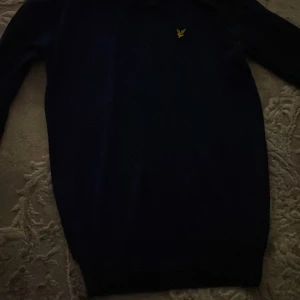 Blå merinoull tröja från Lyle & Scott - Tröjan är M i barn storlek så ungefär 155-165cm passar den. Snygg blå stickad tröja från Lyle & Scott med gul logga på bröstet. Perfekt för dig som gillar klassisk stil med en modern touch. Den är använd ett fåtal gånger.