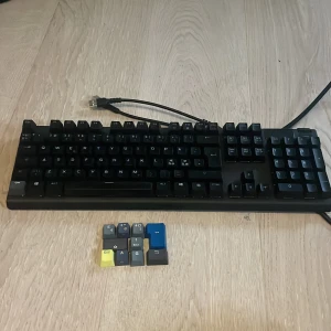 SteelSeries Apex M500 - SteelSeries Apex M500 mekaniskt tangentbord med USB-anslutning. Tangentbordet är i gott skick och levereras med extra färgade keycaps. Perfekt för gaming och skrivarbete. Inga synliga defekter eller större slitage. Kompatibel med PC och har robust byggkvalitet. Röda keycaps som är riktigt bra och låter bra. Man kan ändra färg genom skärmen längst upp i högra hörnet som är riktigt fett Den har också ett stöd för armen/handleden när du spelar som gör det smidigare