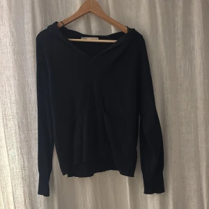 Mörkblå stickad hoodie från ZARA - Mörkblå stickad hoodie från ZARA med två fickor framtill och en bred krage som går över axlarna. Tröjan har långärmade ärmar och en avslappnad passform. Perfekt för dig som gillar enkel och stilren design.