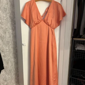 Lång klänning i siden  - Säljer en lång klänning i korall med v-ringning. Baksidan har snygg knyt-detalj och en öppen rygg i siden. Perfekt till bal eller bröllop💕