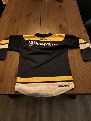 HV71 matchtröja signerad - HV71 hockeytröja med lång ärm, i mörkblått, gult och vitt. Tröjan har tryckta sponsorer och är signerad av spelare på bröstet och ärmarna. Materialet är ventilerande polyester, perfekt för hockey eller samling. Snygg och sportig design med klassiska HV71-loggan. Storlek 110-120 laget säsongen 23-24
