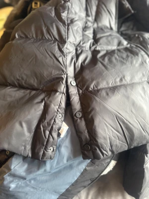 Svart lång dunjacka med huva stl140 eller 10 - Säljer en svart, lång dunjacka med huva och hel dragkedja framtill. Jackan är quiltad och har två sidofickor. Fylld med 50% dun och 50% fjädrar, yttertyg i polyester. Perfekt för kalla dagar och har en clean, oversized look.