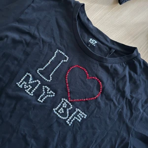 Svart t-shirt  - Svart t-shirt från 157 i storlek L med strassmotiv på bröstet där det står 'I ♥ MY BF'. Hjärtat är gjort av röda strasstenar och texten av silvriga stenar. Tröjan är i grund från lager 157, går att tvätta OBS! Bara i 30 grader, ingen torktumling 