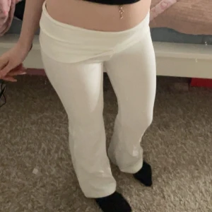 Vita bootcut byxor med omlottmidja - Snygga vita byxor med omlottmidja och bootcut-snitt. De har en mjuk och stretchig passform som sitter skönt på kroppen. Perfekta för dig som gillar trendiga och bekväma plagg med lite extra stil i midjan.