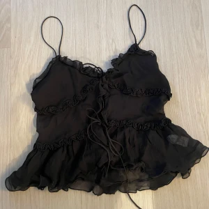 Svart volangtop från Zara  - Säljer nu denna populära slutsålda topp från Zara!!  Toppen har smala axelband och snygga volangdetaljer, med har snörning framtill. Perfekt till en utekväll 🥰