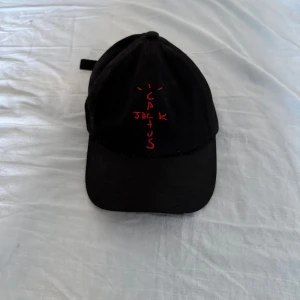 Svart Cactus Jack keps - Svart keps från Cactus Jack med böjd skärm och justerbar rem bak. Framtill finns röd broderad text som bildar ordet 'Cactus Jack' i ett coolt mönster. Kepsen är tillverkad i bomull och har klassisk sexpanelsdesign.