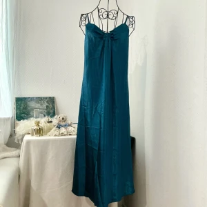 Petrol satinklänning från Morgan Taylor - Säljer en fin petrol långklänning från Morgan Taylor med tunna axelband och snygg knyt-detalj framtill. Storlek S, passar S-M (36-38). Dockan är storlek 34.