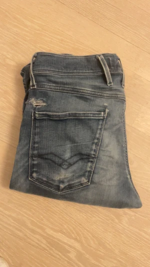 Replay Anbass mörkblå jeans - Snygga Replay Anbass jeans i mörkblå tvätt med klassiska fem fickor. Slim fit-modell med raka ben och låg midja. Jeansen har detaljerade sömmar på bakfickorna och Replay-logga vid fickan fram. Jeansen är lite slitna och därav det lägre priset.