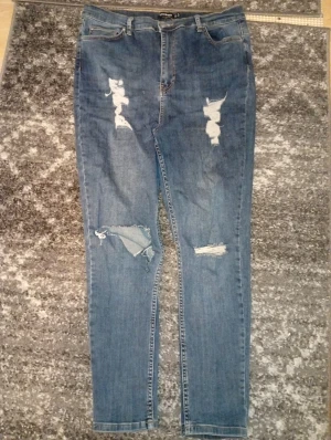 Blå ripped jeans från Boohoo, strl 44 - Säljer ett par blå jeans från Boohoo i storlek 44 med snygga slitningar och hål på framsidan. Modellen har klassisk femficksdesign, hög midja och raka ben. Jeansen är tillverkade i bomull och har en cool, avslappnad vibe.