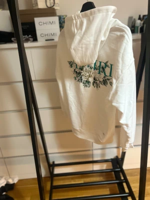 Vit hoodie med blommor från Amiri - Säljer en vit hoodie från Amiri i mjuk bomull med elastan. Tröjan har blommigt tryck och Amiri-logga både fram och bak, stor huva och klassisk magficka. Långärmad och riktigt chill passform, perfekt för dig som gillar stilrena detaljer.