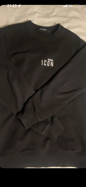 Svart sweatshirt Dsquared2 ICON S - Svart sweatshirt från Dsquared2 i storlek S med vit ICON-print på bröstet. Tröjan har rund hals, ribbade muddar vid ärmslut och nederkant samt långärmad passform. Perfekt för dig som gillar stilrena och trendiga märkesplagg.