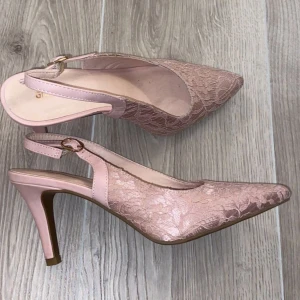 Rosa spetsiga pumps från Graceland - Snygga rosa pumps med spetsig tå och hög klack från Graceland. Skorna har ett romantiskt spetsmönster och en smal rem med guldfärgat spänne runt hälen. Perfekt för dig som gillar feminina detaljer och vill sticka ut med en elegant look.