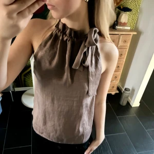 Beige/brun halterneck topp från bubbleroom - Säljer en halterneck topp från bubbleroom i storlek 36. Man kan ha rosetten antingen fram eller bak beroende på hur man vill ha det💗