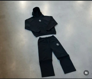 Brasilien dress  - Svarta mjukisbyxor med elastisk midja och vitt tryck på vänster lår. Byxorna har en rak och loose passform, tillverkade i mjukt bomullsmaterial som är skönt att ha på sig. Perfekta för chill eller träning. Snyggt och enkelt streetwear-plagg. Från Joga bonito helt ny 