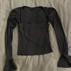 Svart långärmad topp från Gina Tricot - Säljer en svart långärmad topp från Gina Tricot med figurnära passform. Toppen har en snygg, enkel design med slitsdetalj vid ärmsluten och bred, rak urringning. Tillverkad i mjuk bomullsmix som känns skön mot huden.