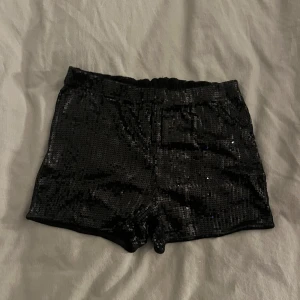 Svarta paljettshorts från H&M - Glittriga svarta shorts från H&M, täckta med paljetter för en riktigt festlig look. De har elastisk midja och är korta i modellen, perfekta när du vill sticka ut. 