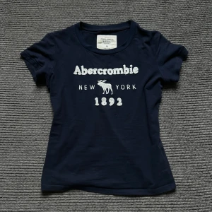 Abercrombie t-shirt  - Snygg mörkblå t-shirt från Abercrombie & Fitch med vit broderad logga och text. storlek M men passar mig perfekt som har XS/S. Skriv om ni har nå funderingar <3