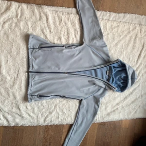 Ljusblå fleecejacka med huva från Houdini - Ljusblå fleecejacka från Houdini med huva och hel dragkedja (i två riktningar ) framtill. Jackan har två sidofickor med dragkedja och är tillverkad i mjuk fleece. Perfekt för lager-på-lager och chill utomhus. Snygga sömdetaljer och diskret Houdini-logga på bröstet. Använd, och vissa tecken på användning syns, se bilder, men tröjan är av väldigt bra kvalitet och inget är trasigt. Inga fläckar. 