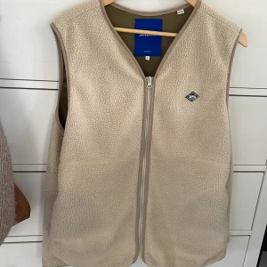 Beige fleeceväst från Jack & Jones - Beige fleeceväst från Jack & Jones med rak passform och hel dragkedja framtill. Västen har en mjuk, teddy-liknande yta och diskret logomärke på bröstet. Perfekt för lager-på-lager och enkel att matcha med andra plagg. Kan tänka mig byta mot nått!
