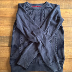 Mörkblå stickad tröja Hampton Republic - Mörkblå stickad tröja från Hampton Republic med klassiskt flätmönster framtill. Tröjan har rund halsringning, ribbade muddar och långärmad passform. Perfekt för dig som gillar en stilren och tidlös look.