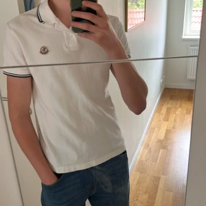 Äkta vit Moncler piké - Säljer en 100% äkta vit pikétröja från Moncler 🔥 Går att verifiera äktheten på monclers hemsida med koden på bild 4. Storlek M men passar S också. Har en liten missfärgning vid kragen som knappt syns (se bild 5) men utöver det inga defekter. Priset är inte satt i sten vid snabbt köp! Hör av er vid frågor 🙌