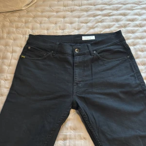 Svarta jeans från Tiger of Sweden 32/32 - Snygga svarta jeans från Tiger of Sweden i modellen Evolve. Klassisk femficksdesign med diskret logga vid fickan och metallknapp framtill. Jeansen har rak passform och är tillverkade i ett mjukt bomullstyg med lite stretch för extra komfort.