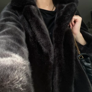 Svart pälsjacka  - Säljer en svart pälsjacka med bred krage och klassisk rak passform. Jackan är fluffig och har en lyxig känsla, perfekt för dig som vill sticka ut. Den är svart och har långa ärmar. Materialet är mjukt och glansigt, vilket ger en riktigt snygg look.
