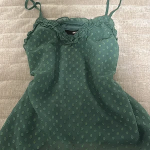 Grön prickig linnetopp från Bik Bok - Snygg grön linnetopp från Bik Bok i storlek XS. Toppen har tunna axelband, volangdetaljer längs halsringningen och ett prickigt mönster i tyget. Materialet känns lätt och luftigt, perfekt för varma dagar. Passar dig som gillar feminina detaljer och chill stil.
