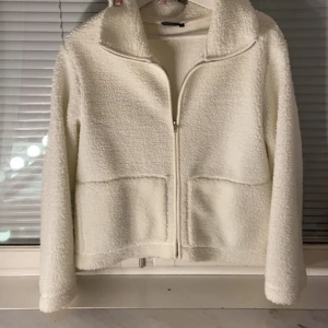Vit teddyjacka med dragkedja - ‼️PRIS KAN SÄNKAS‼️Mysig vit teddyjacka med hög krage och hel dragkedja framtill. Jackan har två stora fickor och är tillverkad i fluffigt fleece-material som ger en skön och trendig look. Perfekt för lager-på-lager och chill vardagsstil.