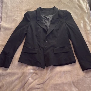 Svart kavaj från Kappahl - Elegant kavaj med klassisk krage, två knappar framtill och fickor med lock. Fodrad insida för extra komfort och en snygg passform. Perfekt för dig som vill ha en clean, tidlös och stilren look ✨  💸 Säljer billigt & brukar acceptera prisförslag – kika gärna på mina andra annonser! 📦 Snabb leverans & rökfritt hem. 