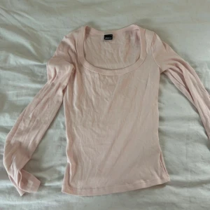 Ljusrosa långärmad topp Gina Tricot - Säljer en ljusrosa långärmad topp från Gina Tricot med rundad, djup urringning. Toppen är i mjuk bomull och har en slim passform som sitter snyggt på kroppen. Perfekt att styla med jeans eller kjol för en enkel och fräsch look.