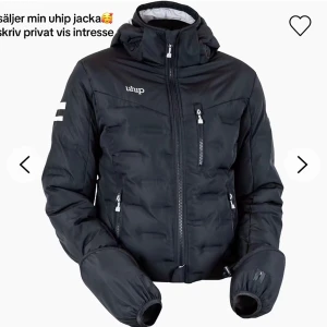 Svart pufferjacka från Uhip - Säljer min svarta pufferjacka från Uhip med huva och flera dragkedjefickor. Jackan har en sportig look med vita detaljer på ärmen och logga på bröstet. Perfekt för kalla dagar och har en skön, normal passform.