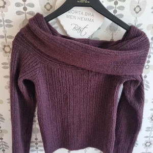 Mörklila ribbad offshouldertröja - Säljer en snygg mörklila stickad tröja med bred offshoulderkrage och ribbad struktur. Perfekt för dig som vill ha en mysig men ändå trendig look. Långärmad och i mjukt material som håller dig varm under kyliga dagar.
