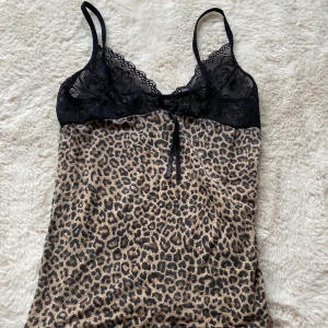 Leopardmönstrad spetslinnetopp - Snygg linne-topp med leopardmönster och svarta spetsdetaljer upptill. Smala axelband och en söt rosett framtill. Perfekt för dig som vill sticka ut med en djurisk vibe. Materialet är mjukt och följsamt, och spetsen ger en extra touch av elegans.