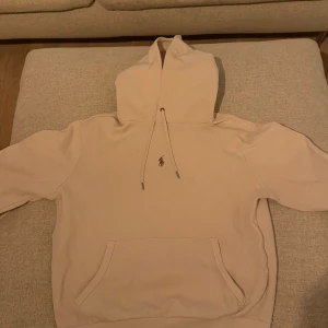 Beige hoodie från Polo Ralph Lauren - Säljer en stilren beige hoodie från Polo Ralph Lauren med klassisk huva och dragsko. Tröjan har en broderad logga på bröstet och en stor magficka framtill. Perfekt för dig som gillar en clean och enkel look.