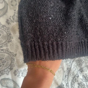 Svart glittrig stickad tröja Cubus - Mysig svart stickad tröja från Cubus med glittriga paljettdetaljer. Tröjan har lång ärm, ribbade muddar och en klassisk rund hals. Perfekt för dig som vill ha något extra till höst och vinter.