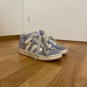 Adidas Campus sneakers ljusblå strl 38 - Snygga Adidas Campus sneakers i ljusblå mocka med klassiska vita ränder och logga på hälen. Skorna har platt sula, rund tå och breda vita snören. Perfekta för dig som vill ha en stilren och trendig look med en touch av retro. Skick bra använda 2 gånger, snörrerna är smutsiga så recomederad att köpa nya fräscha. Orginal pris 1400kr