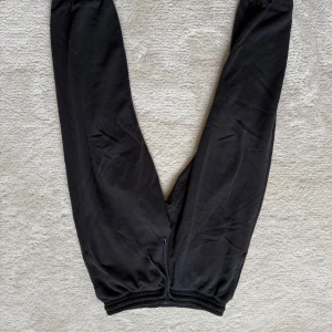 Svarta mjukisbyxor från H&M Relaxed Fit - Svarta mjukisbyxor från H&M med relaxed fit. Byxorna har resår i midjan och vid bensluten för en skön och avslappnad känsla. Perfekta för chill dagar eller när du vill vara bekväm. Tillverkade i mjukt material.