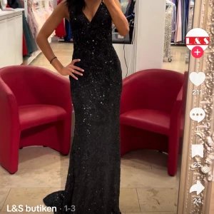  balklänning L&s - Supersnygg svart långklänning med glittriga paljetter och v-ringad hals. Klänningen har en figurnära passform och är ärmlös, perfekt för att sticka ut på bal eller fest. Den eleganta designen ger en lyxig känsla och passar dig som vill glänsa.