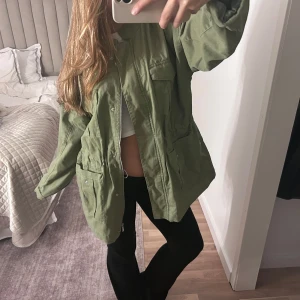 Olivgrön parkajacka med fickor - Säljer en olivgrön bomberjacka med flera stora fickor framtill och dragkedja. Jackan har en loose passform och är tillverkad i bomull. Super varm och skön 