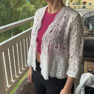 Vit spetskofta från Esmé - Superfin vit kofta i spets från Esmé med vackra broderade detaljer och plisserad volangkant nedtill. Koftan har trekvartsärm och öppen front, perfekt att slänga över en topp för en romantisk look.